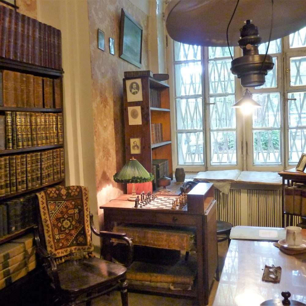La biblioteca e la sua sedia. Accanto, sul tavolo illuminato, la scacchiera. The library and its chair. Next, the lighted table, chessboard