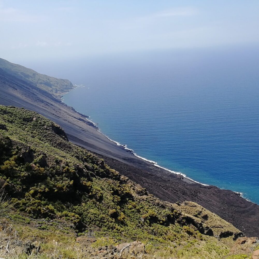 The black lava flow in the side of the crater and in the background the island of Stromboli