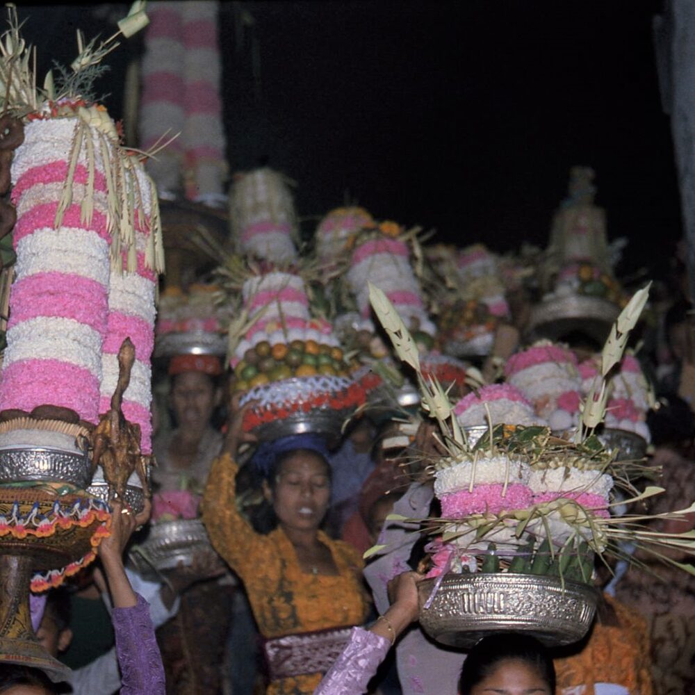 Women carry baskets full of flowers and fruit in their heads
